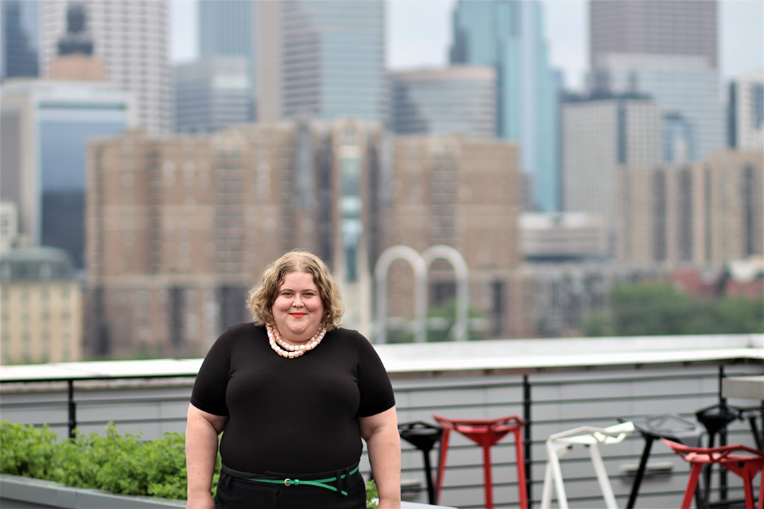 Photograph of Alison Bergblom Johnson, a blonde, plus-size woman in front of the Minneapolis skyline